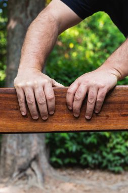 Orta yaşlı bir adamın elleri açık havada, tahta bir kalasın üzerinde, doğal ışıkta. Kopya alanı ile dikey fotoğrafçılık