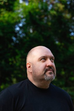 Parkta keçi sakallı kel ve olgun bir adamın gökyüzüne bakan portresi. Açık havada dikey portre doğal ışıkta.