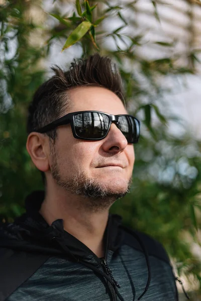 Close-up portrait of a 45-50 years old man wearing sportswear and sunglasses outdoors. Concept of relaxation after sports, confidence and self-confidence