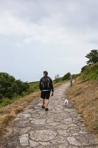 Back view of mature man with backpack walking his dog on a path in nature. Outdoor and lifestyle concept