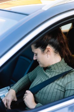 Koyu renk saçlı, 30 yaşında bir kadın arabasının içinde kemerini bağlıyor. Sürüş ve yol güvenliği kavramı