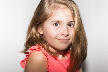 8 yaşında, somon renkli tişört ve açık renk saçlarla kameraya gülümseyen küçük bir kızın yakın plan portresi. Çocuklar ve çocukluk kavramı