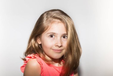 Somon rengi tişört ve açık renk saçlarla gülümseyen 8 yaşındaki küçük kızın yakın portresi. Çocuklar ve çocukluk kavramı