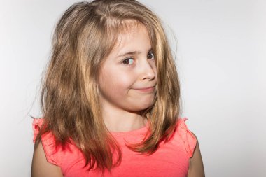 Açık renk saçlı, somon renkli tişörtlü ve beyaz arka planda onaylanmayan bir ifadeyle kameraya bakan çok anlamlı, küçük bir kızın portresi. Çocuk ve çocukluk kavramı