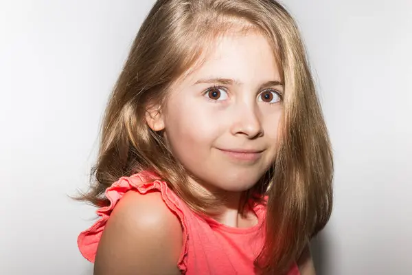 8 yaşında, somon renkli tişört ve açık renk saçlarla kameraya gülümseyen küçük bir kızın yakın plan portresi. Çocuklar ve çocukluk kavramı