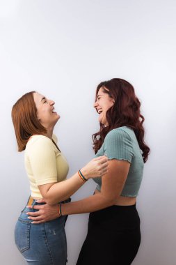 Sıradan giyinmiş, gökkuşağı bilezikleri ve beyaz arka planda güzel manikürleriyle yüksek sesle sarılıp gülen birkaç genç lezbiyen. LGTBI gurur ve haklar kavramı