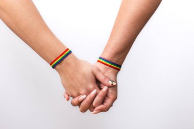 Birleşmiş ellere yakın çekim ve beyaz arka planda gökkuşağı bilezikleri olan lezbiyen bir çiftin güzel manikürü. LGTBI gurur ve LGTBI hakları kavramı
