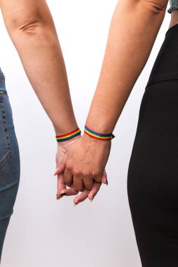 Beyaz arka planda güzel manikür ve gökkuşağı bilezikleriyle el ele tutuşan genç lezbiyen çiftin arka plan görüntüsü. LGTBI gurur ve LGTBI hakları kavramı