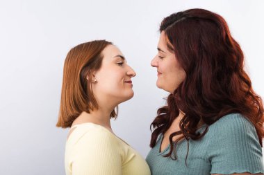 Genç, kızıl saçlı lezbiyen çiftin birbirine aşık bakışları, günlük giysiler giymeleri. Beyaz arka plan. Gurur ve LGTBI hakları kavramı