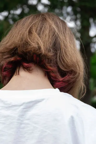 Close-up of red streaked dyed hair of a teenage girl with her back turned outdoors. Concept of hair coloring, highlights and haircut. Beauty and fashion