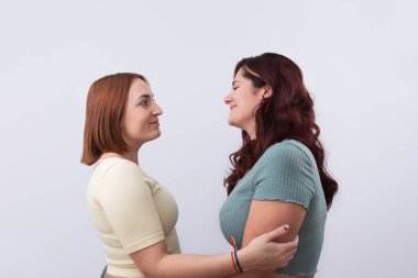 Sıradan giyinmiş, sarılıp gülümseyen ve beyaz arka planda birbirlerinin gözlerinin içine bakan iki genç kızıl saçlı lezbiyen. Gurur ve LGTBI hakları kavramı