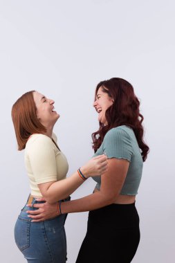 Sıradan giyinmiş, gökkuşağı bilezikleri ve beyaz arka planda güzel manikürleriyle yüksek sesle sarılıp gülen birkaç genç lezbiyen. LGTBI gurur ve haklar kavramı