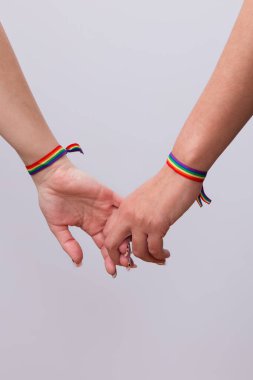 Lezbiyen bir çiftin ellerinin birbirine dolanmış parmakları ve güzel manikürlü, LGTBI bayrak bilezikleriyle yakın çekimi. LGTBI gurur ve LGTBI hakları kavramı