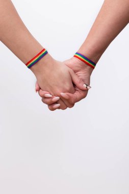 Beyaz arka plan ve fotokopi alanında gökkuşağı bilezikleri olan lezbiyen bir çiftin birleşik ellerine yakın çekim. LGTBI gurur ve LGTBI hakları kavramı