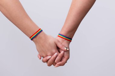 Birleşmiş ellere yakın çekim ve beyaz arka planda gökkuşağı bilezikleri olan lezbiyen bir çiftin güzel manikürü. LGTBI gurur ve LGTBI hakları kavramı
