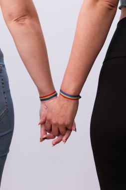 Beyaz arka planda güzel manikür ve gökkuşağı bilezikleriyle el ele tutuşan genç lezbiyen çiftin arka plan görüntüsü. LGTBI gurur ve LGTBI hakları kavramı
