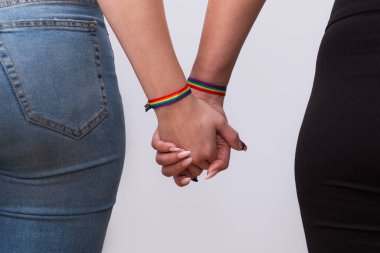 Gayri resmi giyinmiş, güzel manikür ve gökkuşağı bilezikleriyle el ele tutuşan genç lezbiyen çift. LGTBI gurur ve LGTBI hakları kavramı