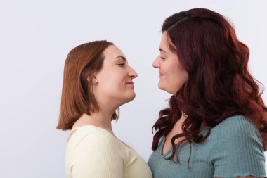 Genç, kızıl saçlı lezbiyen çiftin birbirine aşık bakışları, günlük giysiler giymeleri. Beyaz arka plan. Gurur ve LGTBI hakları kavramı