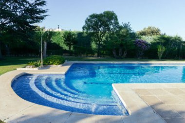 Çimlerle, ağaçlarla ve güneşli bir yaz öğleden sonrasında duşlarla çevrili özel bir bahçede özel bir havuz. Yaz konsepti, sıcaklık ve su