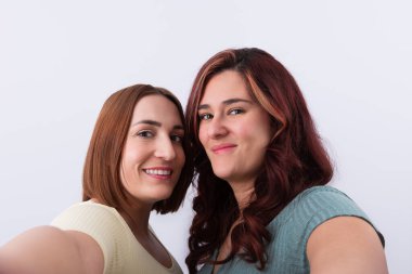 İki tatlı genç bayan arkadaş, arka planda izole edilmiş kameraya bakarak selfie çekiyorlar. Arkadaşlık kavramı