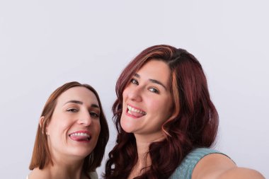 İki genç kız çok yakın arkadaş, komik pozlar veriyorlar, kendi dillerini dışarı çıkarıyorlar ve arka planda hafif bir selfie çekiyorlar. Arkadaşlık ve eğlence kavramı