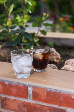 2 bardak buzla dolu, 1 bardak suyla, 1 bardak da meşrubatla, açık havada tuğla bir duvarçiçeğinin üzerinde. Yaz mevsimi kavramı, sıcak ve ferahlatıcı içecek