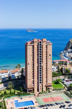 Benidorm, İspanya 'nın Poniente bölgesinde, çok güneşli bir günde arka planda kaya ve mavi denizin olduğu yüksek açılı bir bina. Turizm ve inşaat kavramı