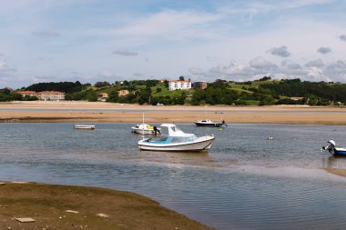 Kuzeyde küçük tekneleri, bulutlu gökyüzünü ve arka planda evleri olan yeşil dağları olan bir nehrin manzarası.