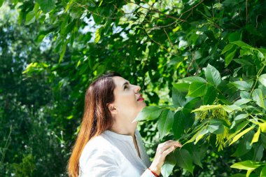 Parkta güneşli bir günün tadını çıkaran, yeşil yaprakları rahat ve mutlu bir şekilde düşünen 45 yaşında olgun bir kadının yatay portresi. Olgunluk, mutluluk ve yaşam tarzı kavramı