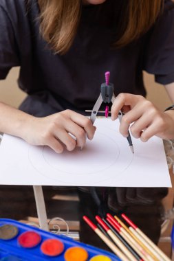 Tanımlanamayan genç bir kız çarşafta pusula ve masada fırçayla daireler çiziyor. Doğal ışık. Yaratıcılık, eğlence ve yaşam tarzı kavramı