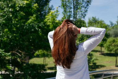 Doğada güneşli bir günde yeşil ağaçlarla çevrili uzun kızıl saçlarına dokunan bir kadın. Uzayı kopyala Sağlıklı yaşam tarzı kavramı