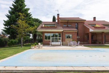 Güneşli bir günde, bahçeli ve havuzlu bir evin önü mavi muşambayla kaplı ve mevsimin dışında suyu koruyan. Mevsimin sonu ya da başlangıcı, sonbahar ya da bahar