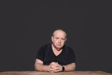 60 yaşında, siyah giyimli, pantolon askısı takmış ve kameraya bakan çok ciddi ve öfkeli bir adam. Karanlık arka plan. Uzayı kopyala Yaşlanma kavramı