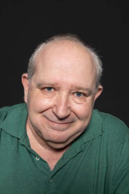 Siyah arka planda gülümseyen kameraya bakan beyaz saçlı ve mavi gözlü 60 yaşında bir adamın portresi. Yaşlanma kavramı