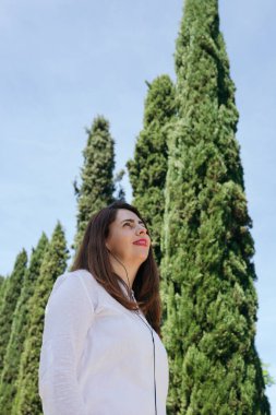 Olgun bir kadın, güneşli bir sabahta gökyüzüne bakıp telli kulaklıklarla müzik dinlerken gülümsüyor. Uzayı kopyala Sağlıklı yaşam tarzı konsepti, kadın ve olgun yaş