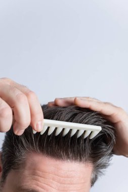 Sıradan giyinmiş yetişkin bir adam peruğunu tararken kameraya bakıyor. Gri arka planda izole edilmiş. Uzayı kopyala Saç şekillendirme ve saç bakım konsepti