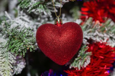 Yeşil ve karlı bir Noel ağacının arka planında kırmızı süslemeler asılı duran kırmızı ve parlak renkte bir kalbin yatay görüntüsü. Duvar kağıdı. Uzayı kopyala Noel konsepti, şenlik ve dekorasyon