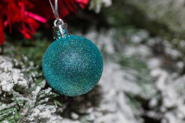 Karlı yeşil bir Noel ağacında asılı duran parlak mavi topun yatay görüntüsü. Arka planda kırmızı süslemeler var. Noel süsü. Duvar kağıdı. Uzayı kopyala Noel konsepti, şenlik ve dekorasyon