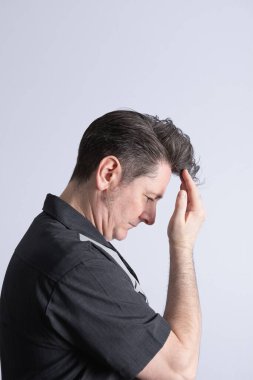 50 yaşında, peruklu bir adamın profili, ciddi bir ifadeyle saçına dokunuyor. Tarafsız bir arka plan, rahat bir tutum. Kişisel bakım ve erkek modası kavramı