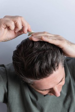 Peruğunu elleri ve tarağıyla tarayan bir adama yaklaş. Gri arka planda izole edilmiş. Saç şekillendirme ve saç bakım konsepti