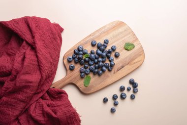 Tahta tahtadaki taze yaban mersininin üzerinde nane yaprakları ve tarafsız arkaplanda kırmızı kumaş var. Uzayı kopyala Doğal ve zarif bir stil. Sağlıklı yemek yapma, tazelik ve sağlık kavramı