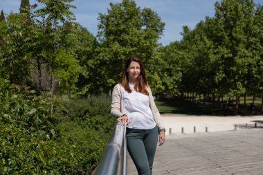 Olgun ve kendine güveni tam bir kadın, açık bir günde yeşil bir köprüde poz veriyor. Uzayı kopyala Güçlendirme, denge ve doğa ile uyum kavramı