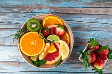 Portakal dilimleri, greyfurt, limon, kivi ve çilek dilimli kasenin en üst görüntüsüne çilekler ayrı bir kasede eşlik ediyor. Mavi kırsal arka plan. Uzayı kopyala Sağlıklı beslenme ve tazelik kavramı