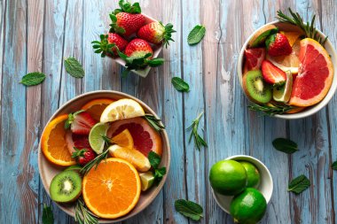 Limon dilimleri, portakallar, greyfurt ve çilekler kırsal mavi arka planda kaselerde sıralanmış. Canlı ve ferahlatıcı bir görüntü. Yaz kavramı, doğal yiyecekler ve vitaminler