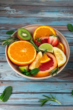 Bir kase portakal, limon, greyfurt, çilek ve kiviyle birlikte mavi kırsal masada taze otlar. Sağlıklı beslenme ve tazelik kavramı