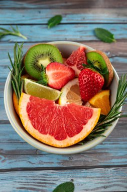 Taze meyve, greyfurt, çilek, kivi, kivi, limon ve portakalın biberiye ve nane yapraklarıyla süslenmiş renkli karışımı. Doğal malzemeler ve canlı dokular. Beslenme, yaz ve sağlık kavramı