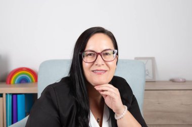 Çalışma alanında olgun bir kadın, zarif siyah beyaz giysiler içinde, eli çenesinde kameraya gülümsüyor. Uzayı kopyala Güven, liderlik ve mesleki başarı kavramı