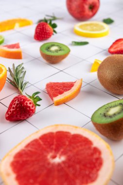 Geometrik arka planda greyfurt, çilek, kivi ve limon gibi taze meyveler. Seçici yaklaşım dokuları ve canlı renkleri vurguluyor. Sağlıklı beslenme ve tazelik kavramı