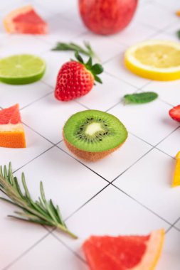 Minimalist beyaz fayanslı arka planda turunçgiller ve çileklerle çevrili taze yarım kivi. Canlı ve ferahlatıcı bir kompozisyon. Sağlıklı yeme kavramı