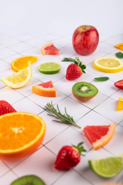 Beyaz yüzeyde şebeke ile sanatsal düzende çeşitli meyveler. Kivi, çilek, limon, portakal, greyfurt, limon, elma ve biberiye. Taze ve parlak bir görüntü. Dengeli beslenme ve sağlık konsepti